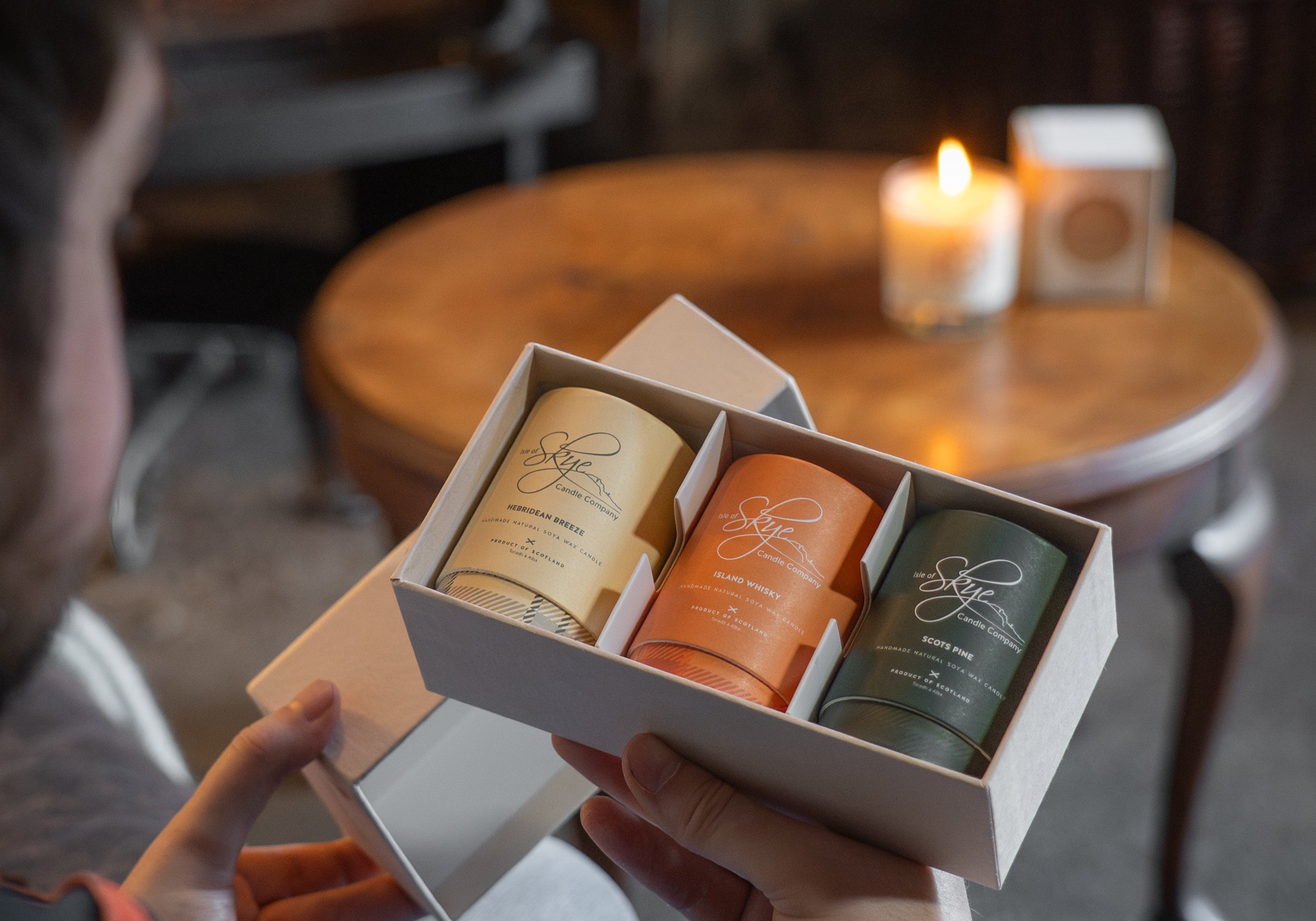 Male holding Isle of Skye candle gift set in a cosy pub environment. Gift set features three miniature candles. 